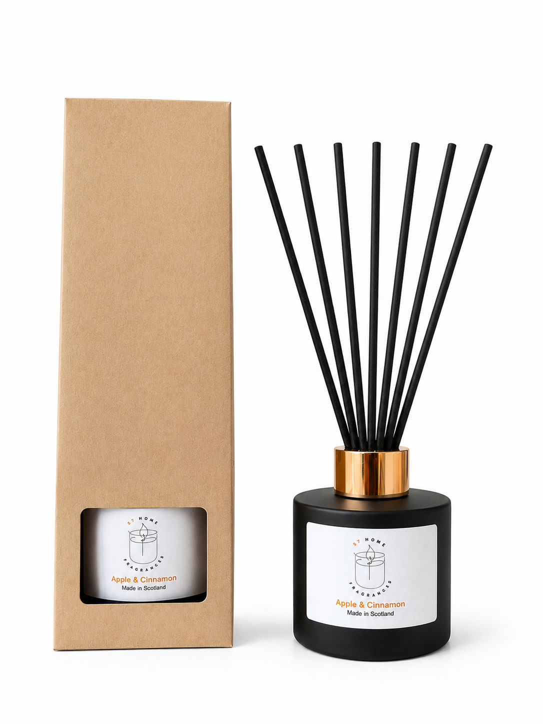 A reed diffuser bottle with black reeds and a black glass base next to its tall brown kraft paper box. The bottle has a white label with a simple line drawing of a gift box and the text 'Apple & Cinnamon' and 'Made in Scotland'.