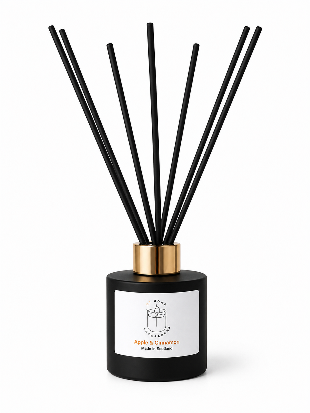 A reed diffuser bottle with a matte black cylindrical base, a metallic gold collar, and multiple black reed sticks, shown on a clean white background. The front label reads 'Apple & Cinnamon' and 'Made in Scotland'.