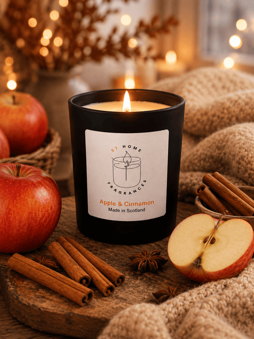 Candle labeled 'Apple & Cinnamon' surrounded by apples and cinnamon sticks on a wooden surface.