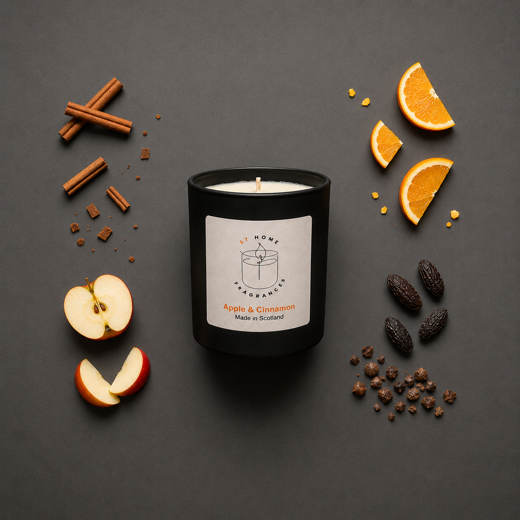 Black candle labeled 'Apple & Cinnamon' surrounded by fruit and spices on a dark background