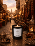 A black scented candle with a white label reading 'S7 Home Fragrances' and 'Arabian Souk' sits on an ornate bronze table in a detailed, warmly lit Middle Eastern market street scene.