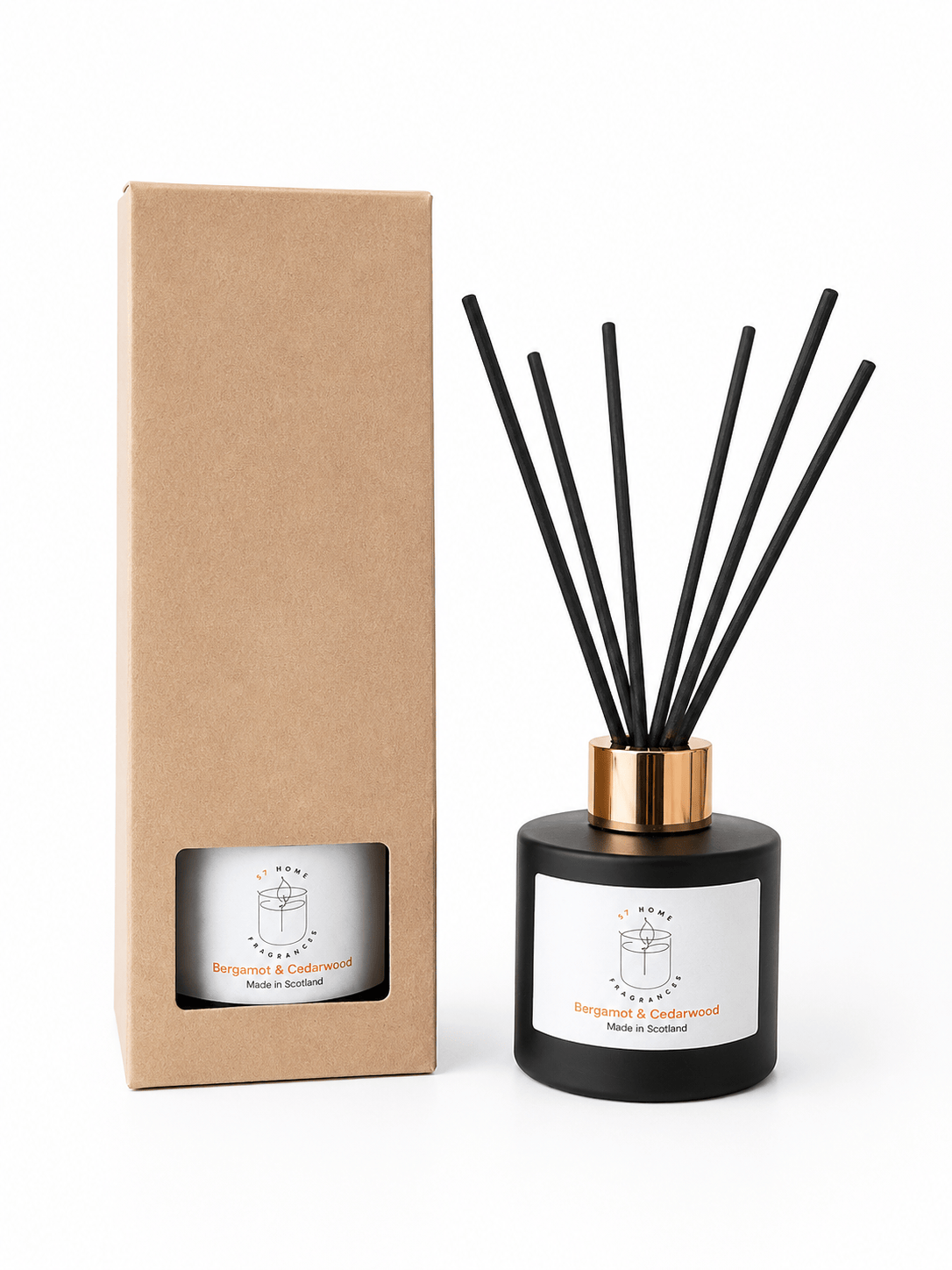 A reed diffuser bottle with black reeds, a black glass body, and a gold collar stands next to its plain brown cardboard box on a white background.