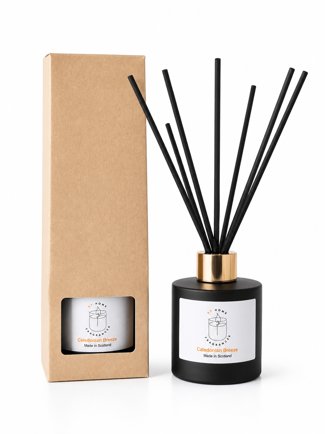A reed diffuser bottle with black reeds and a gold collar stands next to its brown kraft paper box on a white background. The bottle has a white label with a simple line drawing and the text 'Caledonian Breeze' and 'Made in Scotland'.