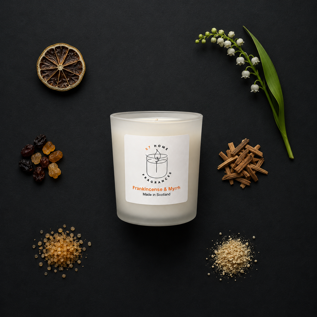 Frankincense & Myrrh Scented Candle with a label surrounded by dried fruits, flowers, and herbs on a dark background