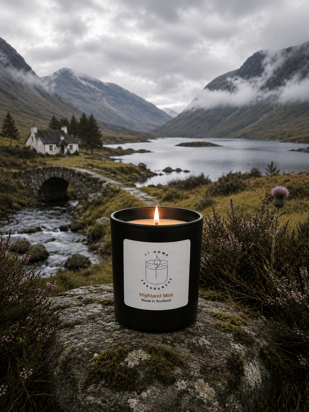 A black candle jar with a white label reading 'Highland Mist' sits on a mossy rock in a mountain landscape with a lake, bridge, and cloudy sky.
