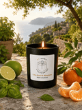 Lime basil & mandarin candle in a black jar and white label, made in Scotland in a setting with fruit overlooking a Tuscany view