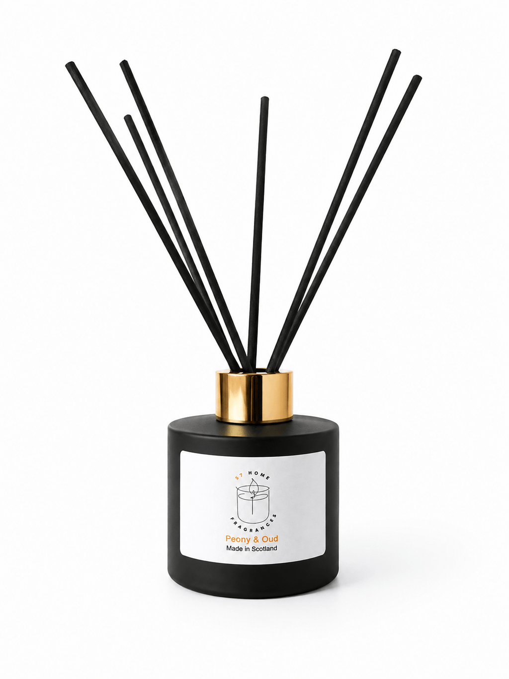 A reed diffuser bottle with a matte black cylindrical body, a white front label, and a shiny gold collar, with several black reed sticks extending upward on a white background.