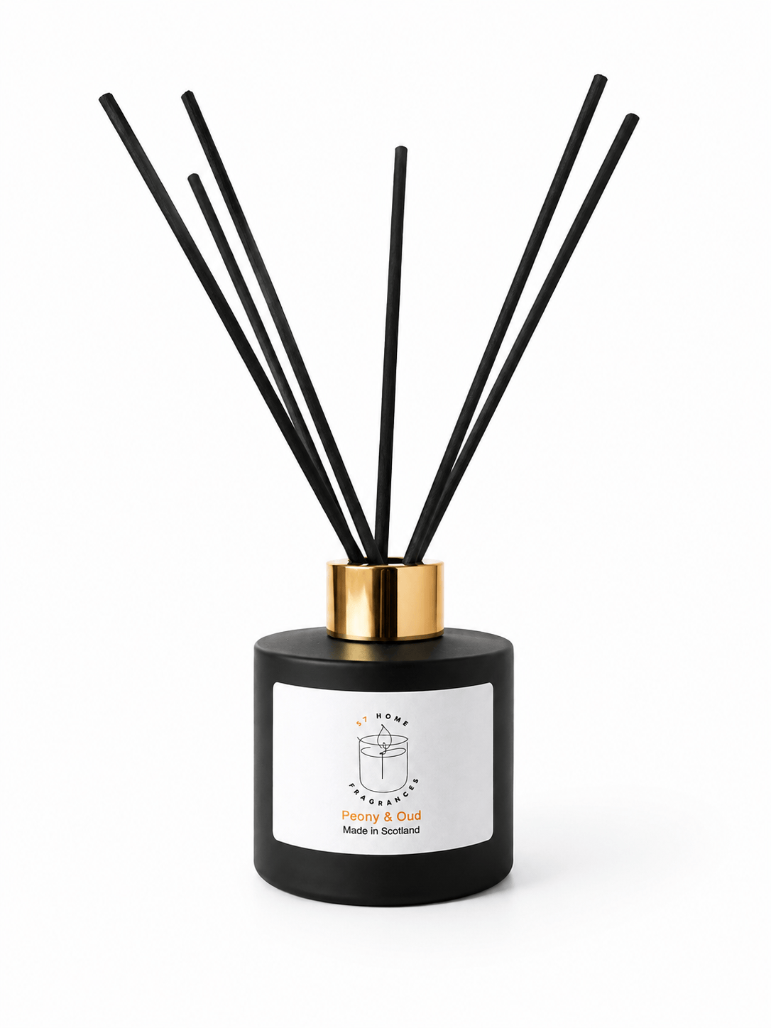 A reed diffuser bottle with a matte black cylindrical body, a white front label, and a shiny gold collar, with several black reed sticks extending upward on a white background.