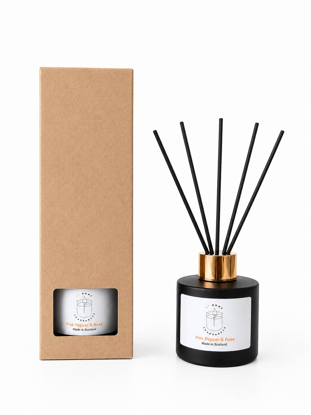 A reed diffuser bottle with black reeds and a gold collar stands next to its tall brown kraft paper box on a white background. The bottle has a white label with a minimalist logo and text.