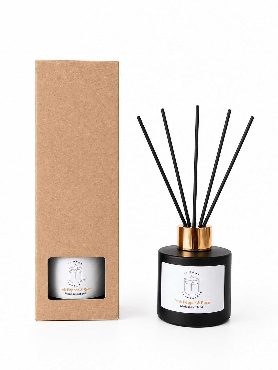 A reed diffuser bottle with black reeds and a gold collar stands next to its tall brown kraft paper box on a white background. The bottle has a white label with a minimalist logo and text.