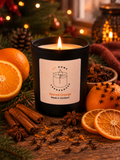 Black soy candle jar labelled 'Spiced Orange Made in Scotland' surrounded by orange slices, cinnamon sticks and cloves on a wooden surface