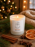 White soy candle jar labelled 'Winter Spice Made in Scotland' styled on a wooden surface with Christmas decorations, cinnamon sticks and pine cones